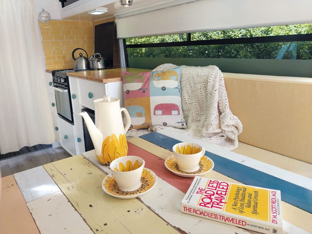 Motorhome interior showing mutil-coloured handmade table with teacups, jug and book